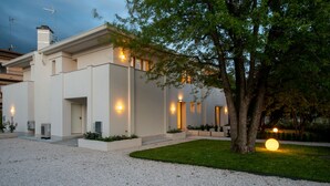 A modern house with a gravel driveway, a well-maintained lawn, and a tree in the foreground.