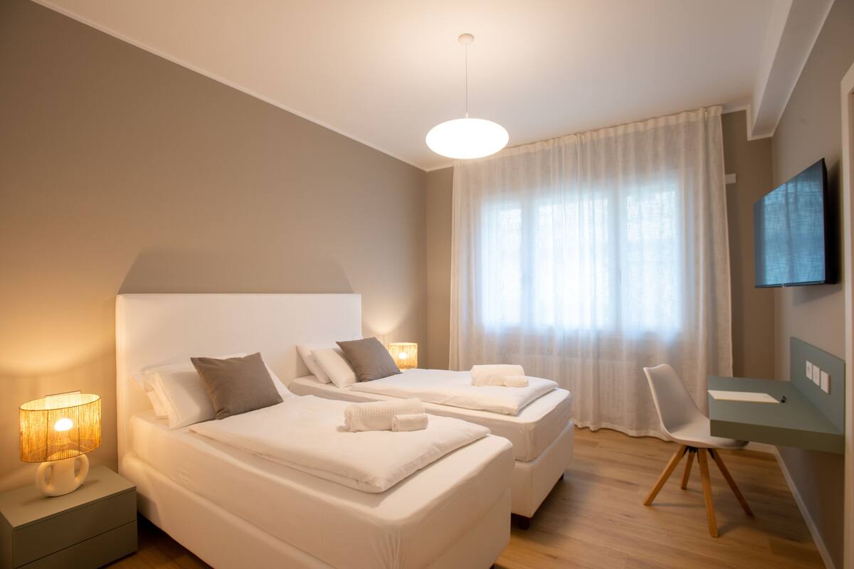 Ein modernes Hotelzimmer mit zwei Betten, einem Schreibtisch und einem Fernseher.