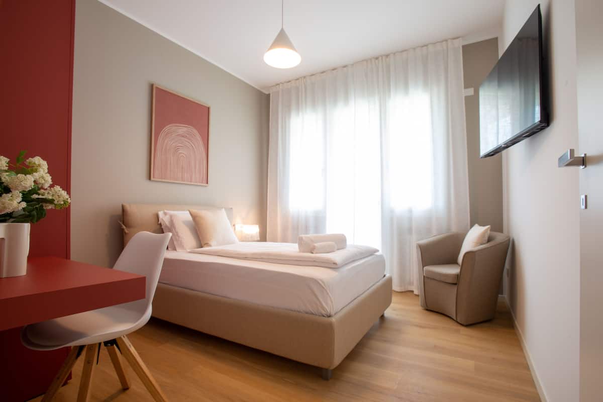 Ein modernes Hotelzimmer mit einem Bett, einem Schreibtisch, einem Sessel und einem an der Wand montierten Fernseher.