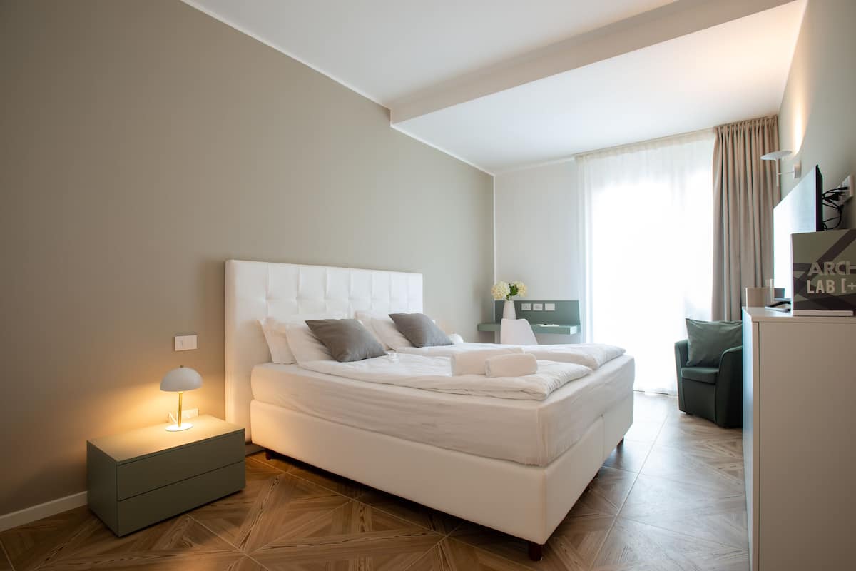 Ein modernes Hotelzimmer mit einem großen Bett, einem Nachttisch mit Lampe, einem Schreibtisch und einem Stuhl.