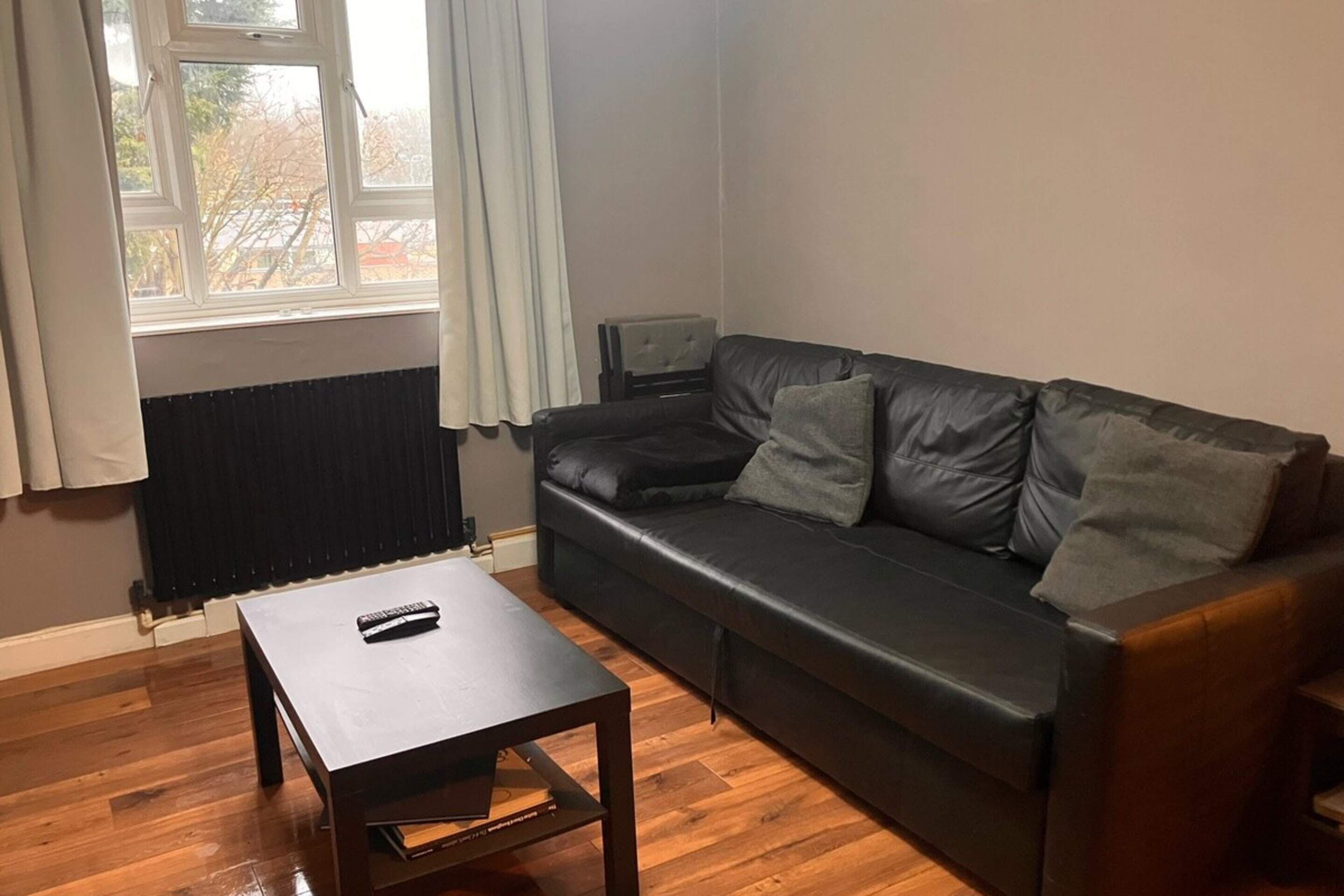A living room with a black leather sofa, a wooden coffee table, and a window with curtains.