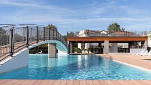 En swimmingpool med ett trädäck, ett böjt metallräcke och en överbyggd sittplats med solstolar.
