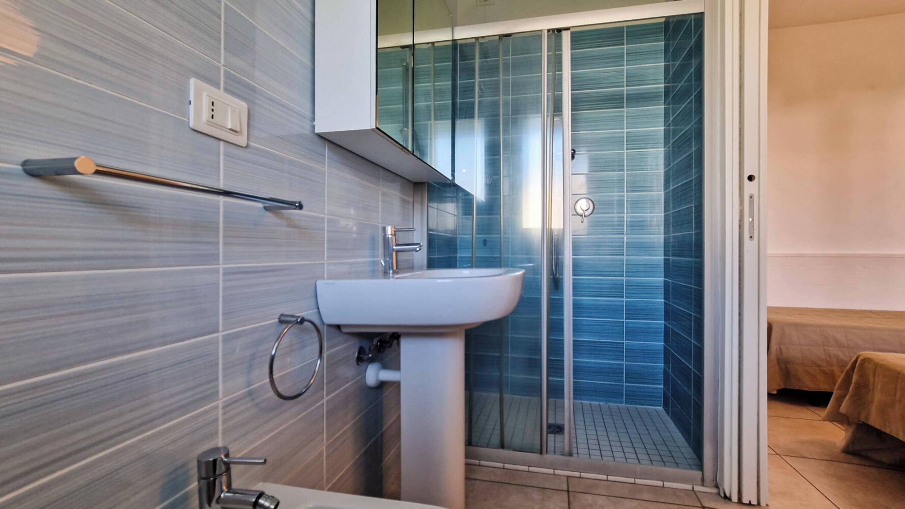 Een moderne badkamer met een witte wastafel, een douchecabine van glas en een handdoekrek.