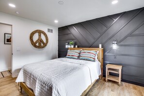 Een slaapkamer met een bed, een klein houten nachtkastje, een aan de muur bevestigd vredesteken en een muur met een geometrisch patroon.