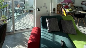 A modern living room with a green sofa, red ottoman, and a dining area with a table and chairs. - Bright 1BD Flat W/balcony - Heart of Brixton! (London)