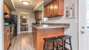 A kitchen with wooden cabinets, a black refrigerator, a granite countertop, and two bar stools. - Woodford Stables / Walk to Eckert's Orchard (Versailles)
