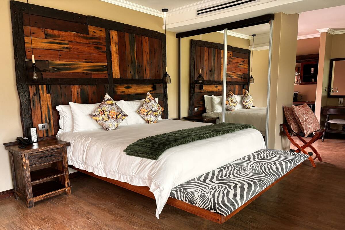 A large bed with a zebra-patterned pillow, a wooden headboard, and a green throw blanket.