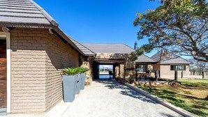 A house with a brick exterior, a stone facade, and a paved driveway leading to a covered outdoor area. - Shekinah Lion and Game Lodge  (Vaalwater)