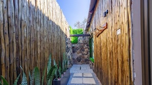 A narrow pathway flanked by wooden walls with a stone wall and greenery in the center. - Shekinah Lion and Game Lodge  (Vaalwater)