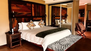 A bedroom with a large bed, a wooden headboard, a bedside table with a lamp, and a chair. - Shekinah Lion and Game Lodge  (Vaalwater)