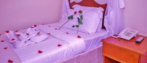 A bed with a white bedspread, a wooden headboard, and a bedside table with a telephone and remote control.