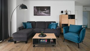 A modern living room with a sectional sofa, a teal armchair, a wooden coffee table, a floor lamp, and a framed picture on the wall.