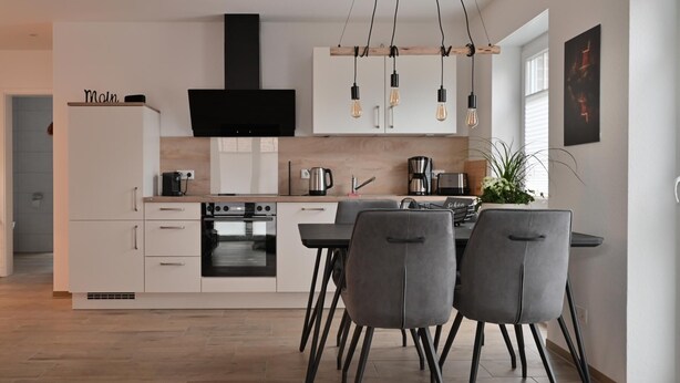 A modern kitchen with a built-in oven, a dining area with a table and chairs, and a large window providing natural light.
