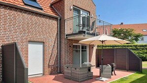 A brick house with a balcony, a covered patio with outdoor furniture, and a dog.