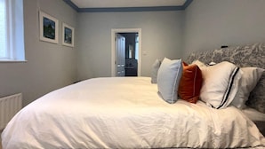 Een slaapkamer met een groot bed, een hoofdbord met een patroon en twee ingelijste foto’s aan de muur.