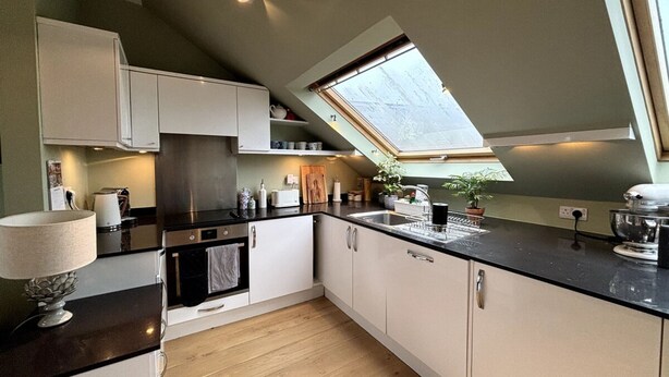Een moderne keuken met dakraam, houten vloer en witte kastjes.