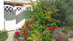 A white building with a gated entrance, surrounded by a variety of flowering plants.