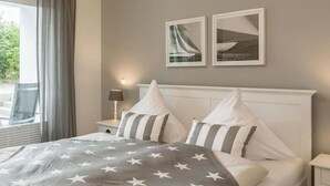 A neatly arranged bedroom with a bed, pillows, a nightstand, and two framed pictures on the wall.