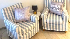 Two striped armchairs with pillows, a small side table, and a wall-mounted shelf with a plant and decorative items.