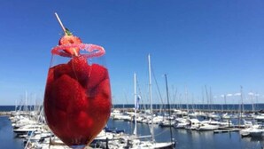 A glass of red drink with a strawberry garnish, set against a marina with boats in the background.