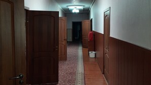 A hallway with wooden doors, a patterned carpet, and a ceiling light fixture. - Hotel Sezim (Toktogul)