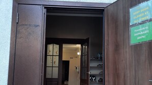 An open wooden door leading to a hallway with a shoe rack and a sign indicating the door should be kept closed at all times. - Hotel Sezim (Toktogul)