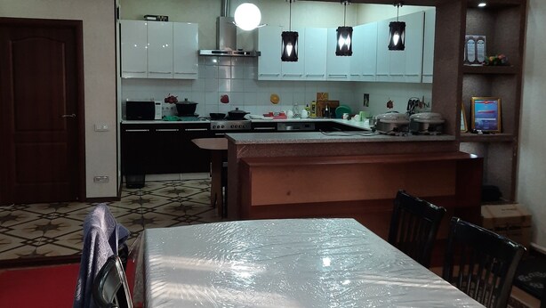 A modern kitchen with white cabinets, a central island, and pendant lighting. - Hotel Sezim (Toktogul)