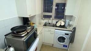 A compact kitchen with a stove, microwave, and washing machine. - Cosy Studio Flat - 12 Mins to British Museum! (London)