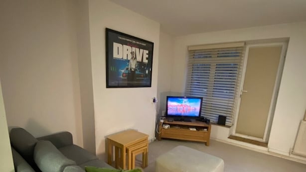 A living room with a grey sofa, a small wooden table, a television, and a poster on the wall. - Cosy Studio Flat - 12 Mins to British Museum! (London)