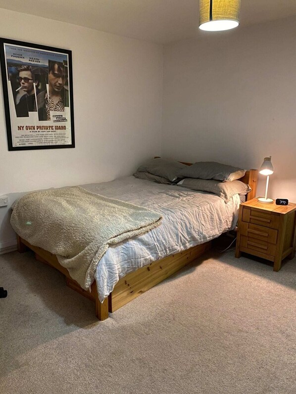 A single bed with a wooden frame, a bedside table with a lamp, and a poster on the wall.