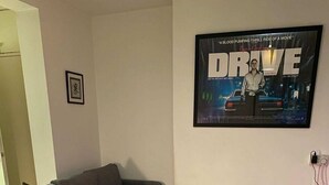 A living room with a grey sofa, a small ottoman, and a framed movie poster on the wall. - Cosy Studio Flat - 12 Mins to British Museum! (London)