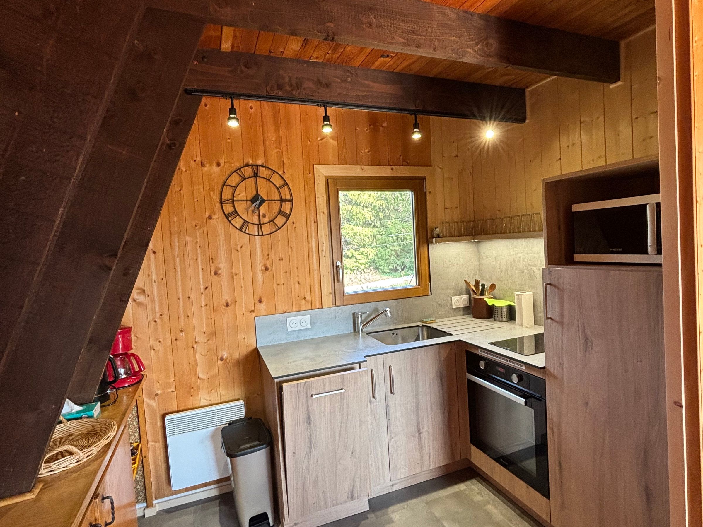 A compact kitchen with wooden walls, a window, a microwave, and a sink.