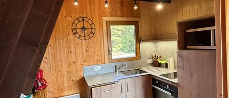 A compact kitchen with wooden walls, a window, a microwave, and a sink.