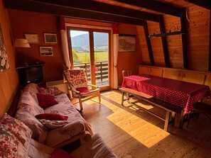 A cozy room with a sofa, a chair, a table with a red tablecloth, a television, and a view of the outdoors through a glass door.