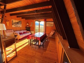 A cozy room with a wooden ceiling, a bed, a dining table, and a bench.