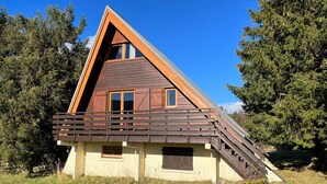 Una cabaña de madera triangular con techo inclinado, un balcón y una ventana pequeña.