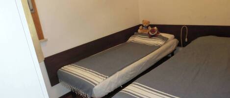 A small, single-room accommodation with two single beds, each with a striped blanket.