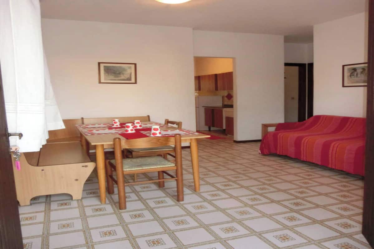 A small, cozy room with a dining table, chairs, a sofa, and a kitchen area.