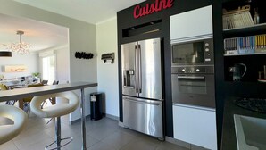 A modern kitchen with a stainless steel refrigerator, double oven, and a bar area with stools.