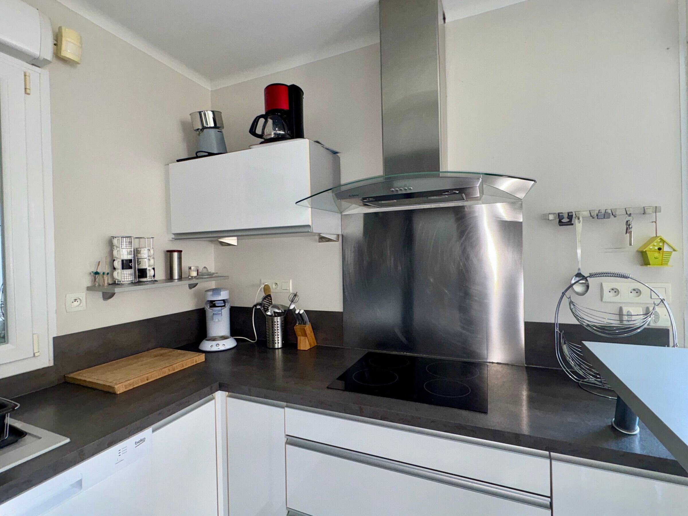 A modern kitchen with a stainless steel range hood, a built-in oven, and a coffee maker on the countertop.
