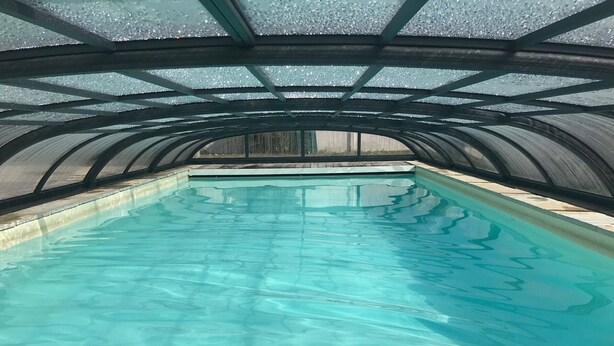 An indoor swimming pool with clear water, surrounded by a curved metal roof structure.