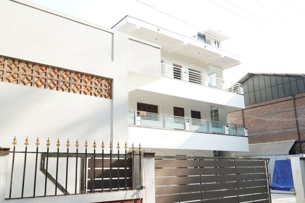 A modern two-story building with a white facade, a balcony on the upper floor, and a gated entrance.