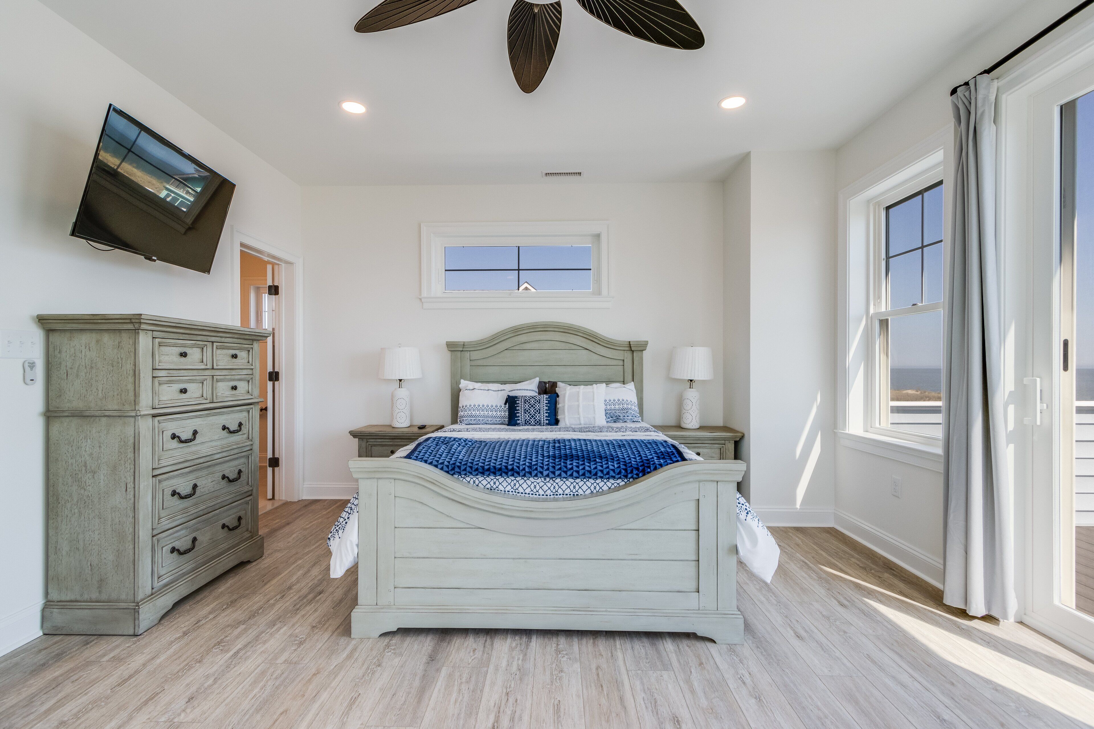 A bedroom with a bed, dresser, TV, and a window with curtains.