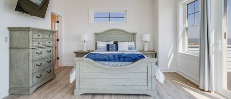 A bedroom with a bed, dresser, TV, and a window with curtains.