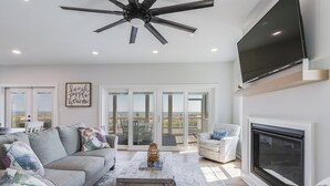 A modern living room with a ceiling fan, a flat-screen TV, a fireplace, and a large window overlooking a deck. - 510 S. Bayshore Dr.- 4 Bedroom Waterfront home located in Broadkill Beach, with Spectacular Views! (Milton)