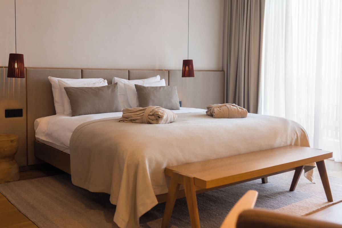A modern hotel room with a large bed, a wooden bench, and two pendant lights.