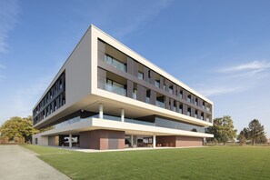 A modern multi-story building with a flat roof, large windows, and a spacious outdoor area with a lawn. - Hotel Materra (Cepin)