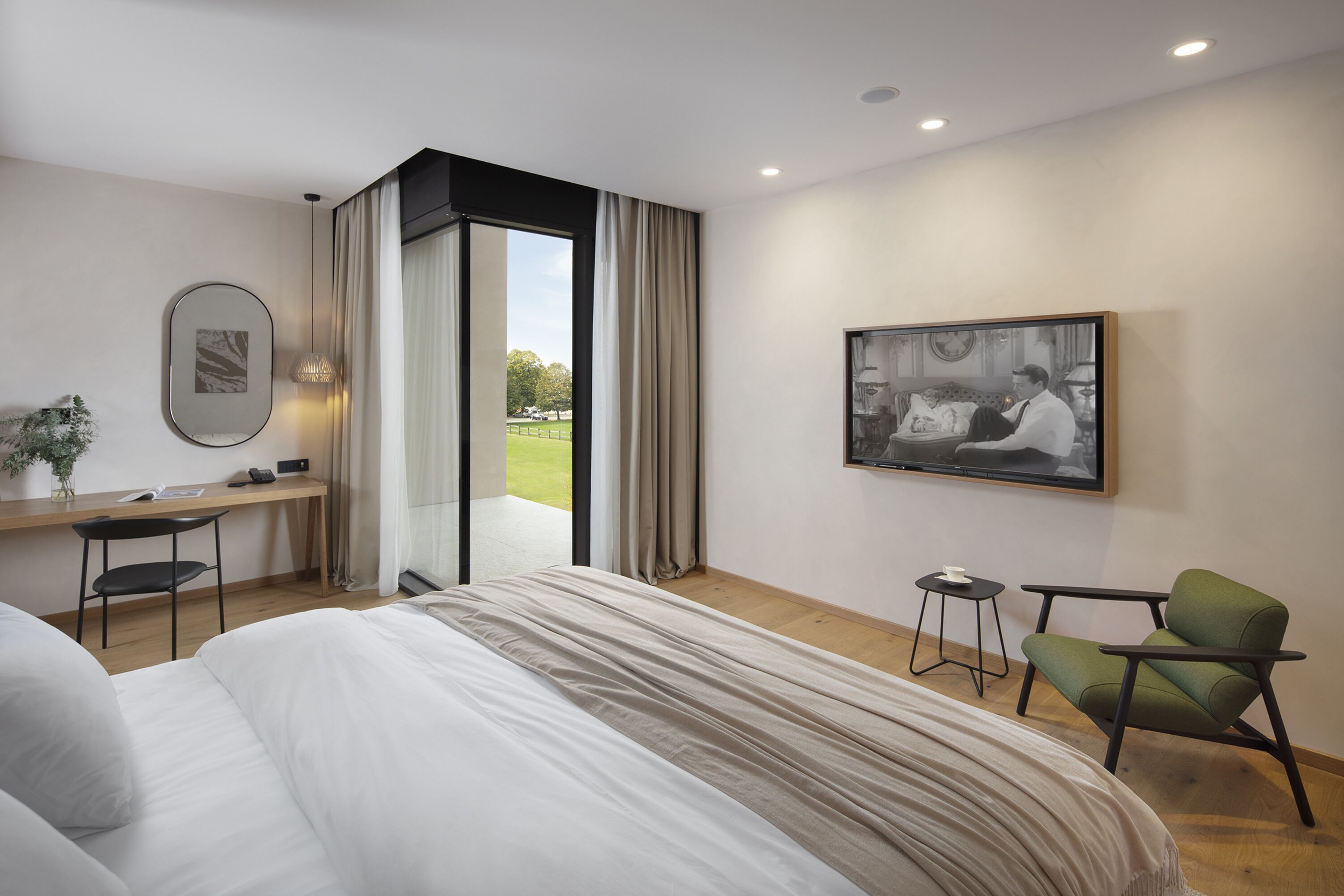 A modern hotel room with a large bed, a desk, a chair, and a view of the outdoors.