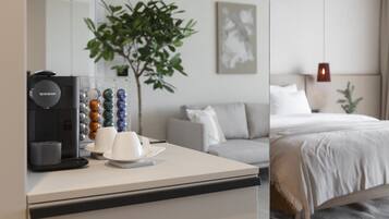 Habitación de hotel con cafetera, una planta, una cama y un cuadro en la pared.