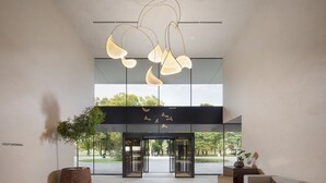 A modern lobby with a glass entrance, a minimalist sofa, and a hanging light fixture. - Hotel Materra (Cepin)